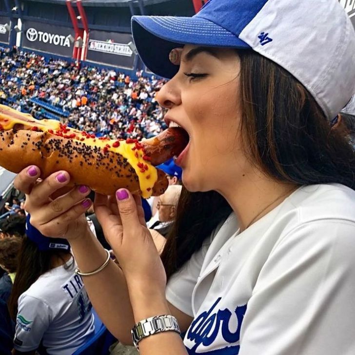 Fan eating a cheesy hotdog messily